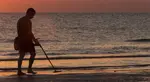 Man metal detecting on beach at sunset